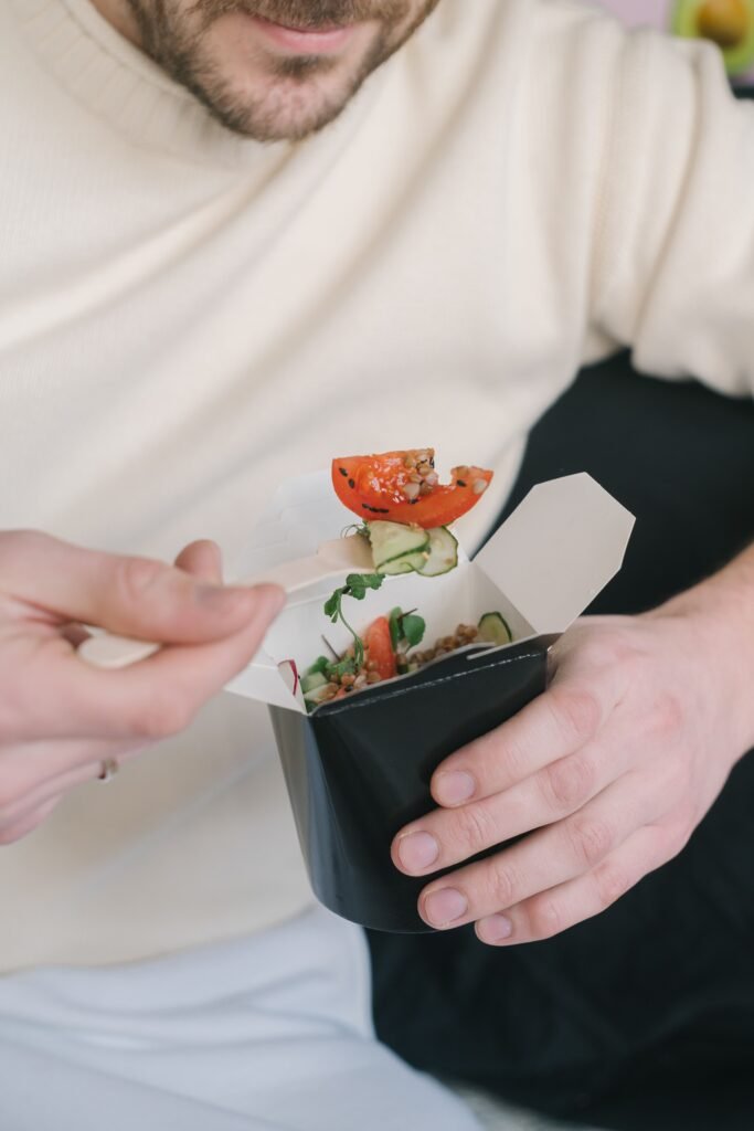 Close-up of a man eating a fresh salad from a takeout box, emphasizing healthy eating.