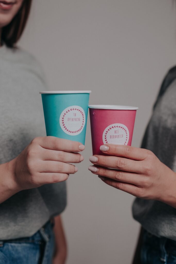 Close-up of two women with manicured hands holding colorful paper cups indoors.